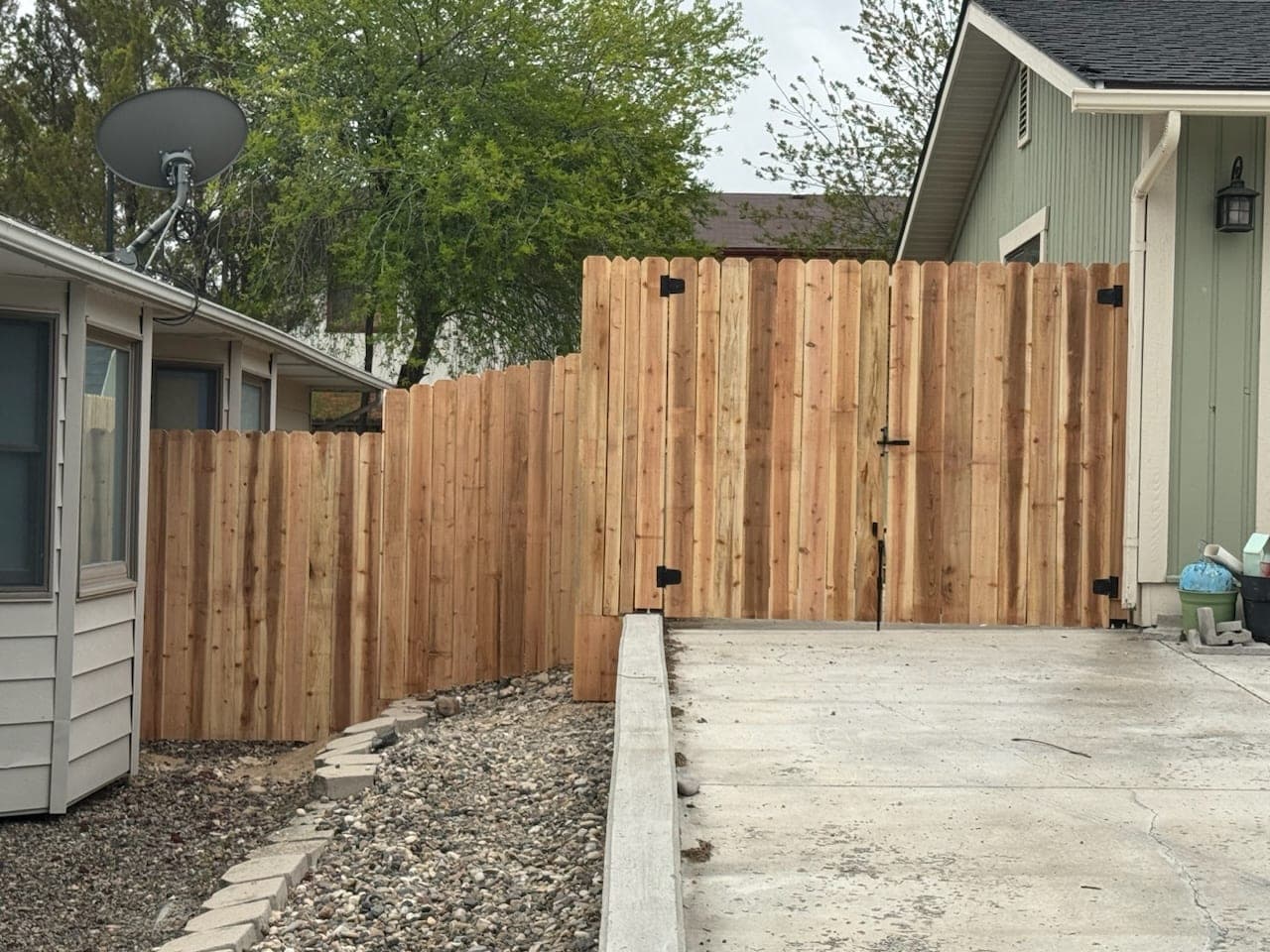 Dog-ear cedar privacy fence with a double gate across a concrete driveway between two homes, Elko, Nevada