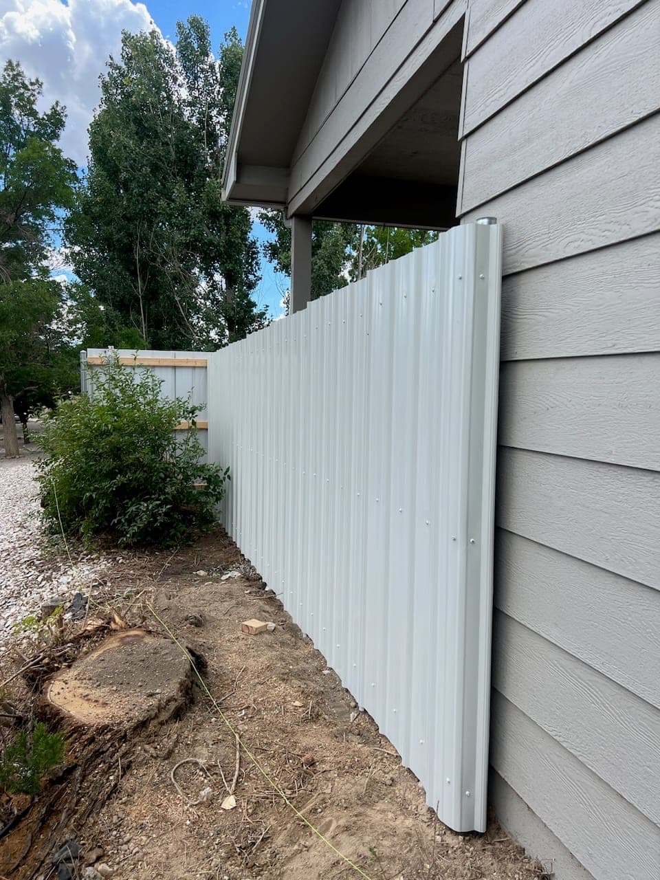 Corrugated steel privacy fence panels on steel posts against a gray house, Elko, Nevada