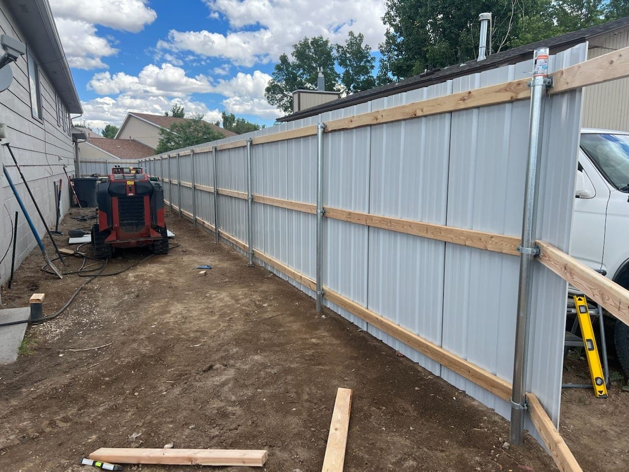 Corrugated steel fence with wood rails and steel posts during installation along a side yard, Elko, Nevada