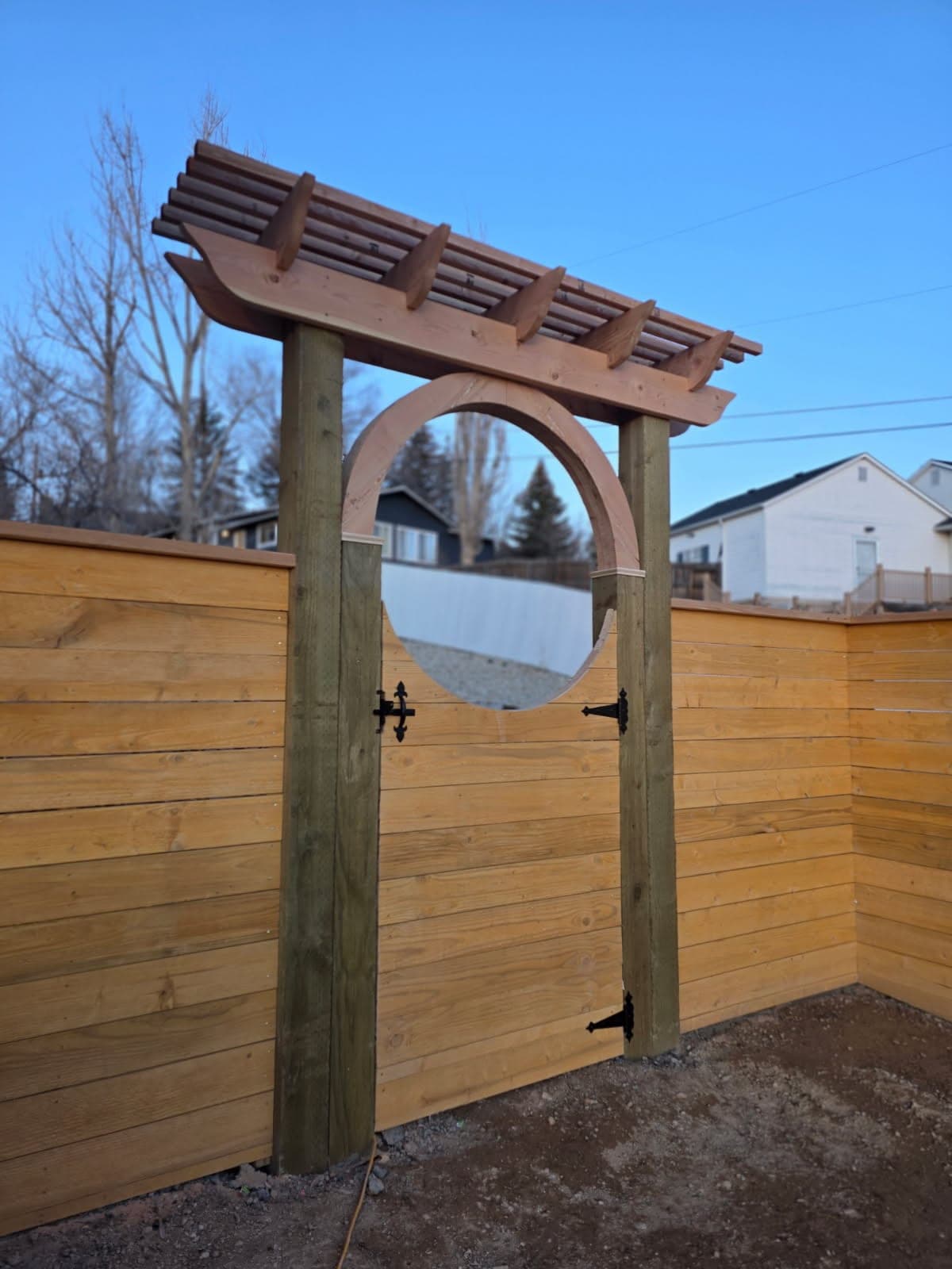 Round moon gate cut into a horizontal cedar fence with overhead cedar beams, Elko, Nevada