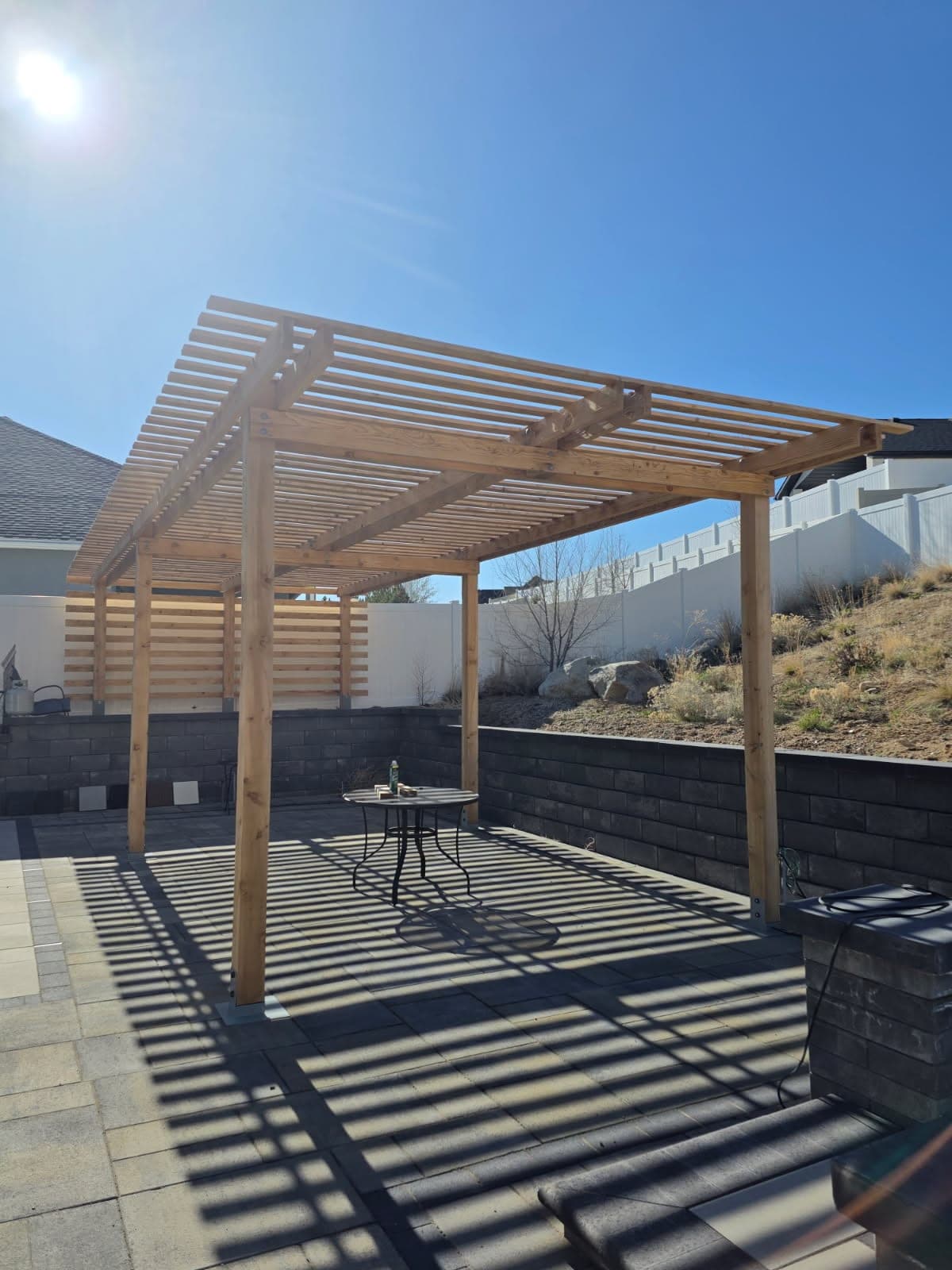 Cedar pergola casting slatted shade over a paver patio with a block retaining wall, Elko, Nevada