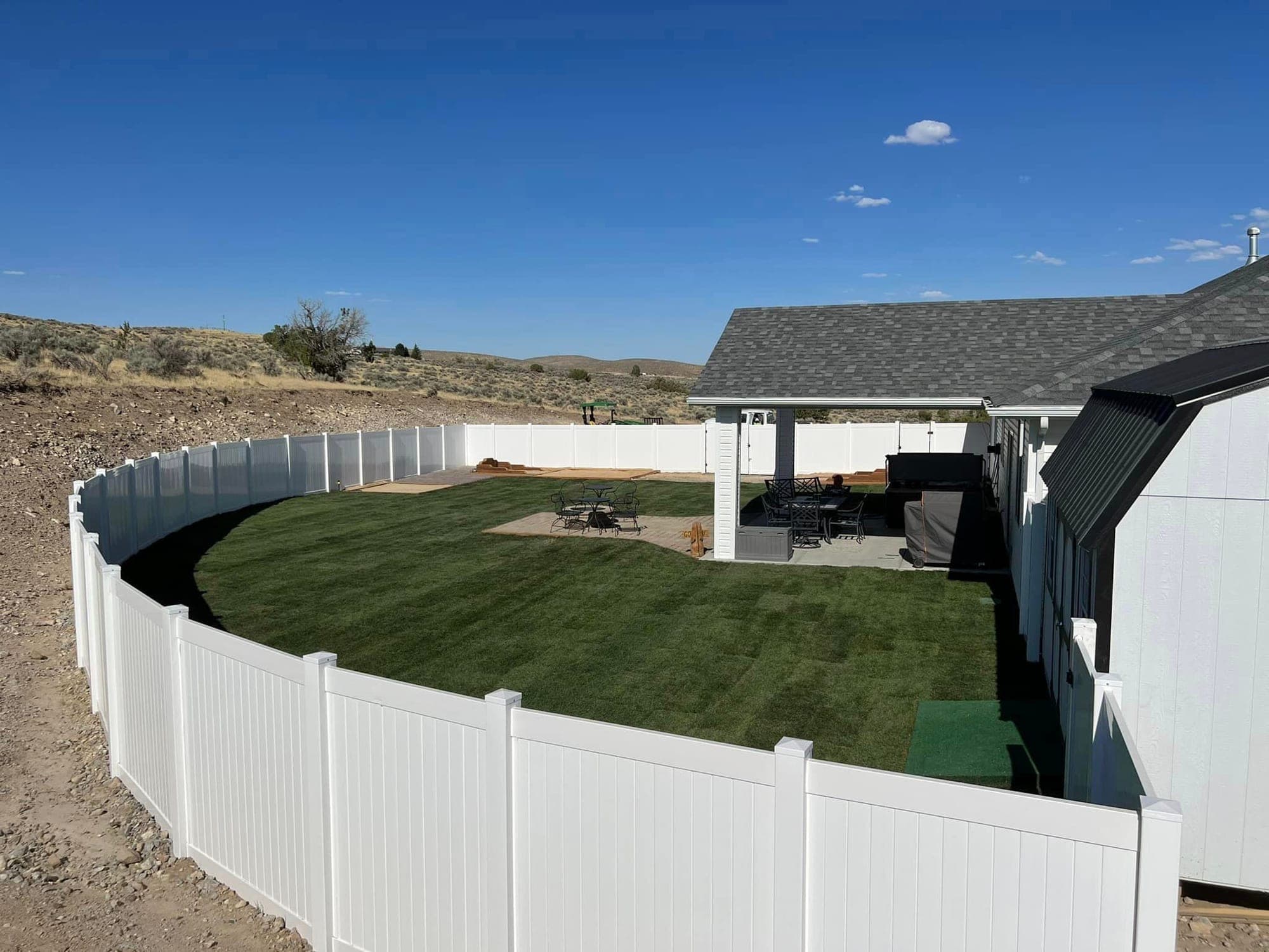 Curved white vinyl privacy fence around a new sod lawn and covered patio on a hilltop lot outside Elko, Nevada