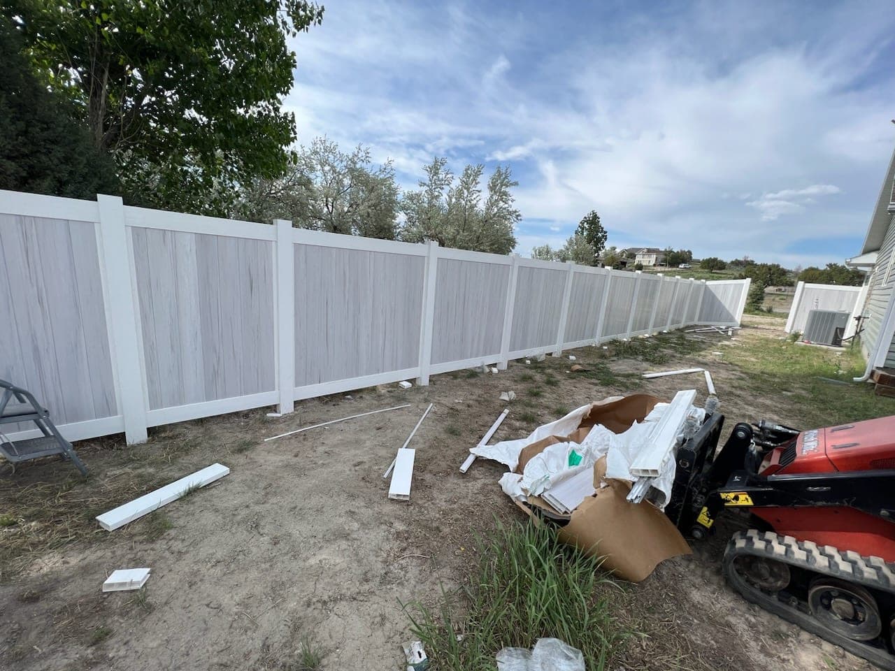 Gray woodgrain vinyl privacy fence with white posts during installation in Elko, Nevada